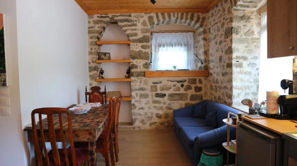 Το πέτρινο σαλόνι κουζίνα του Tsagariko Rooms με τα ξύλινα ράφια